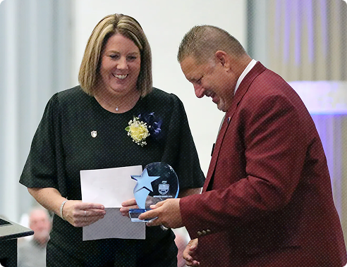 Image A smiling woman receives a trophy at the Summit County Sports Hall of Fame annual banquet honoring local athletics.